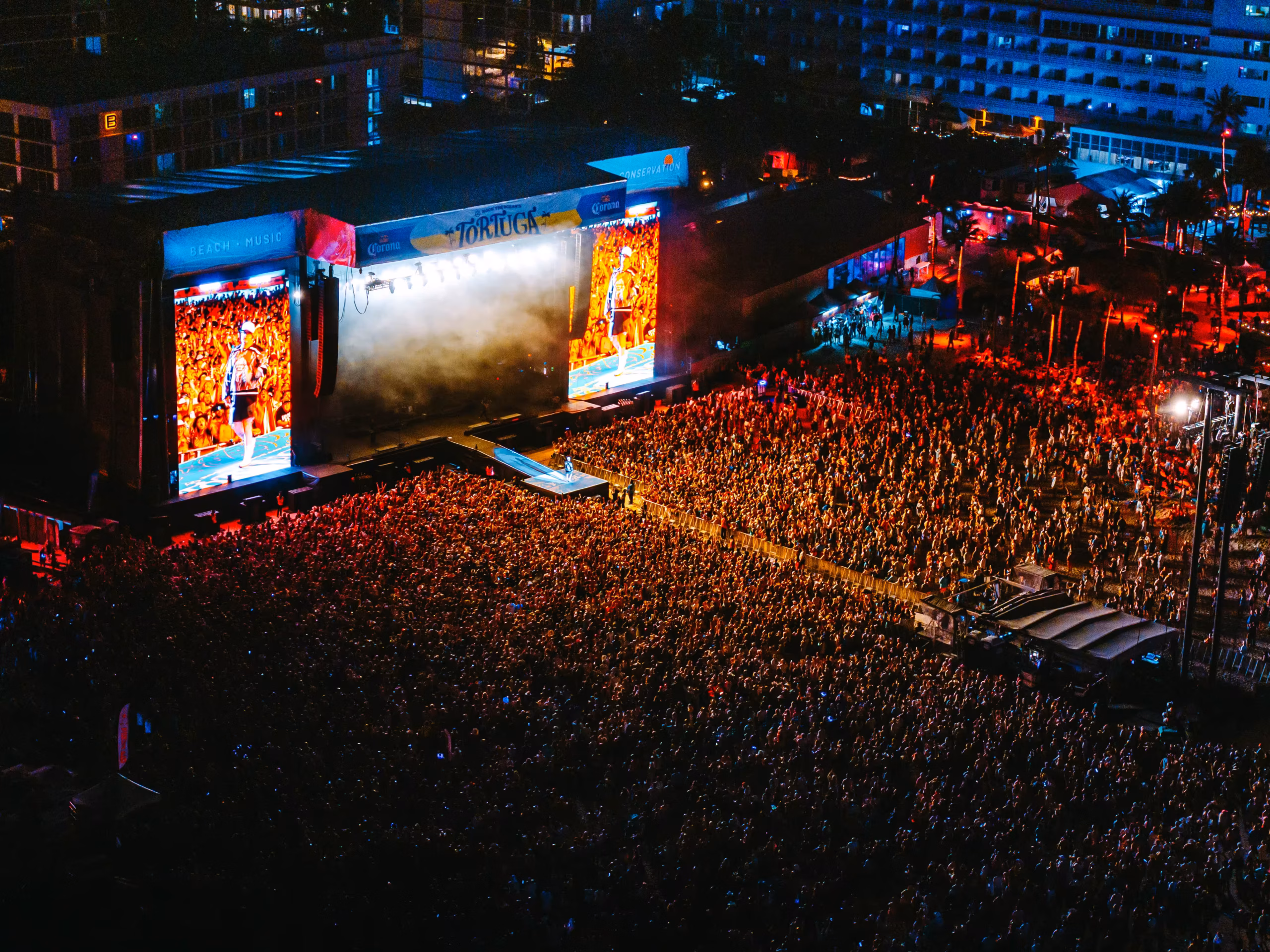 Aerial view of the Tortuga Music Festival main stage at night with massive LED screens illuminating the crowd on Fort Lauderdale Beach