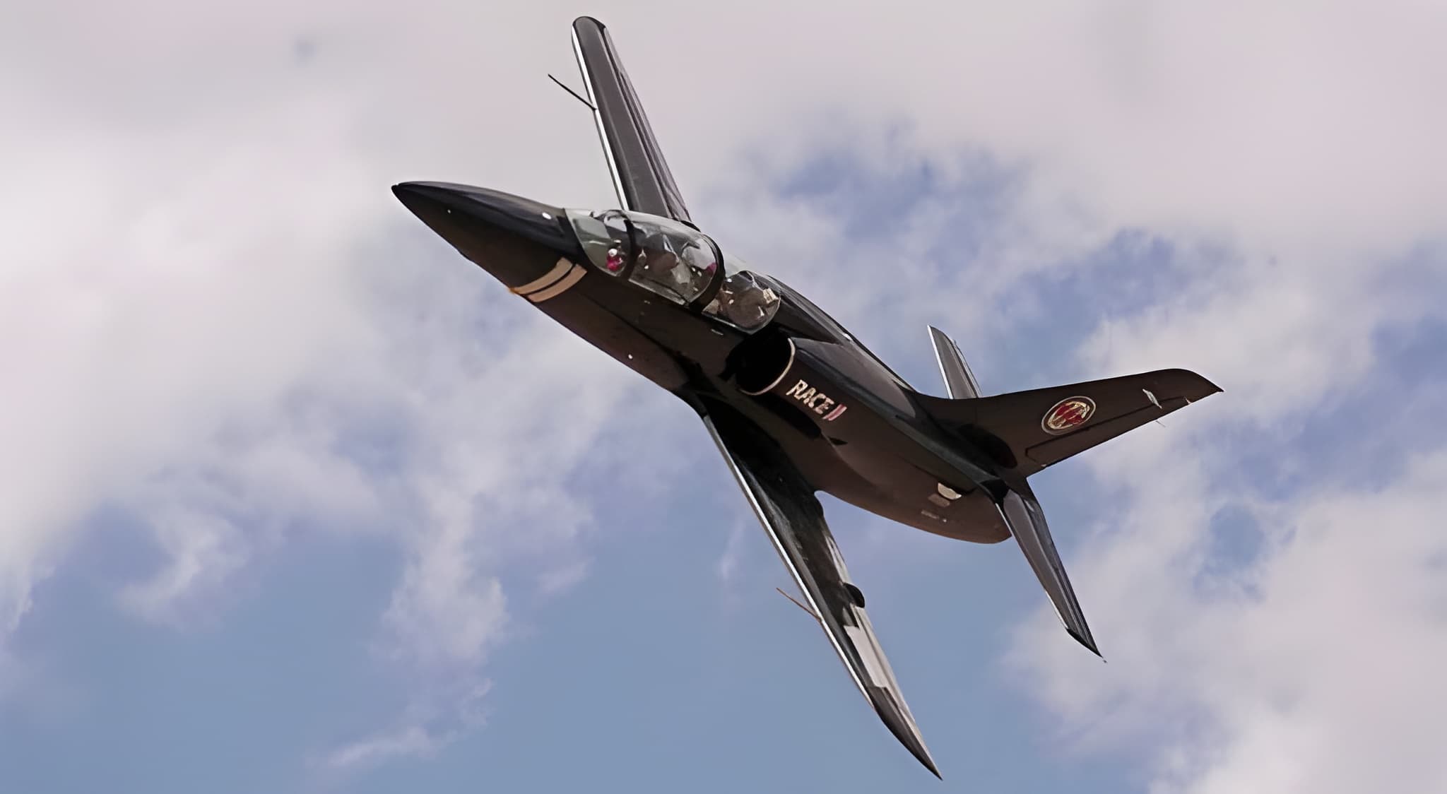 Sleek black twin-seat jet aircraft banking steeply against a cloudy sky during an aerobatic demonstration