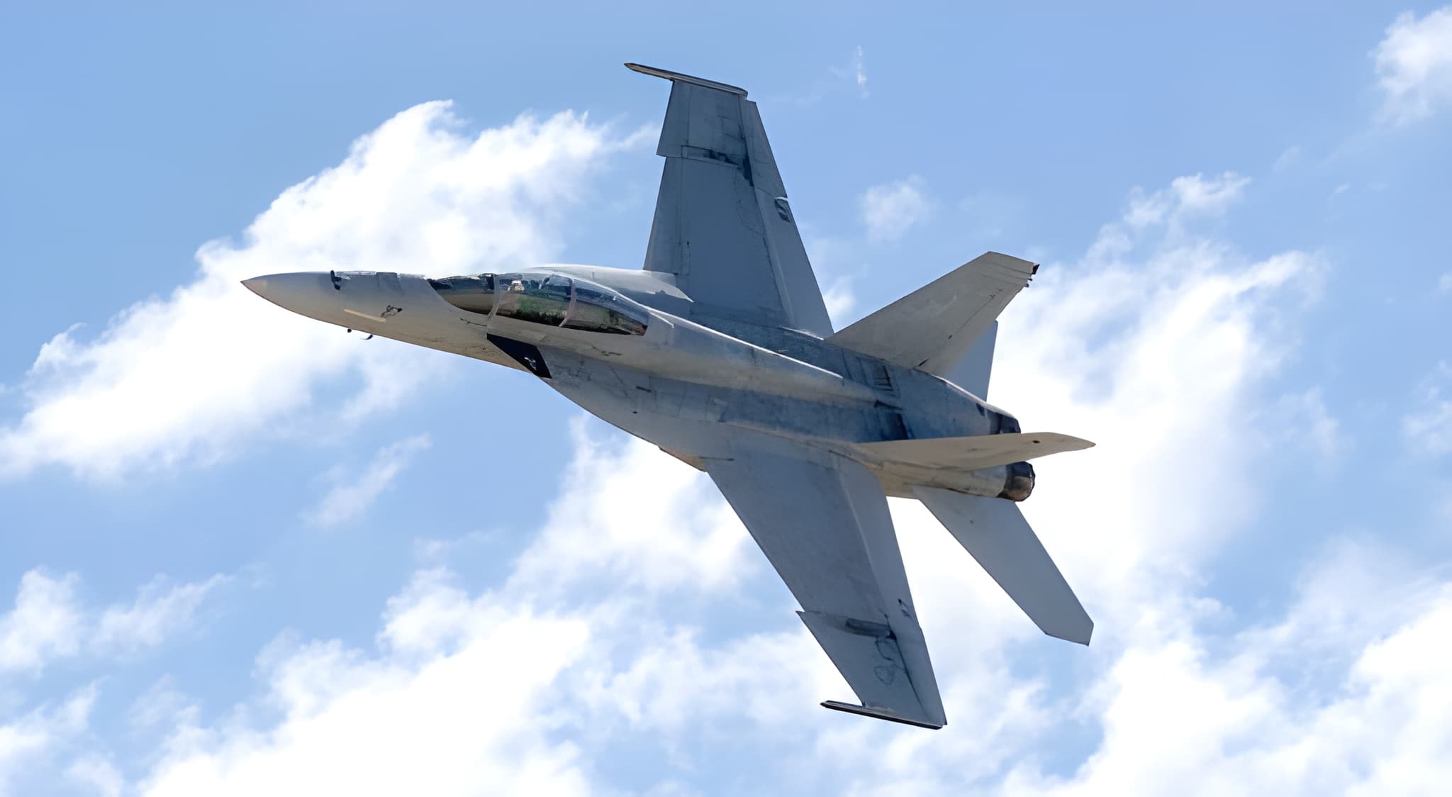 U.S. Navy F/A-18 Super Hornet in grey livery banking left against a partly cloudy sky