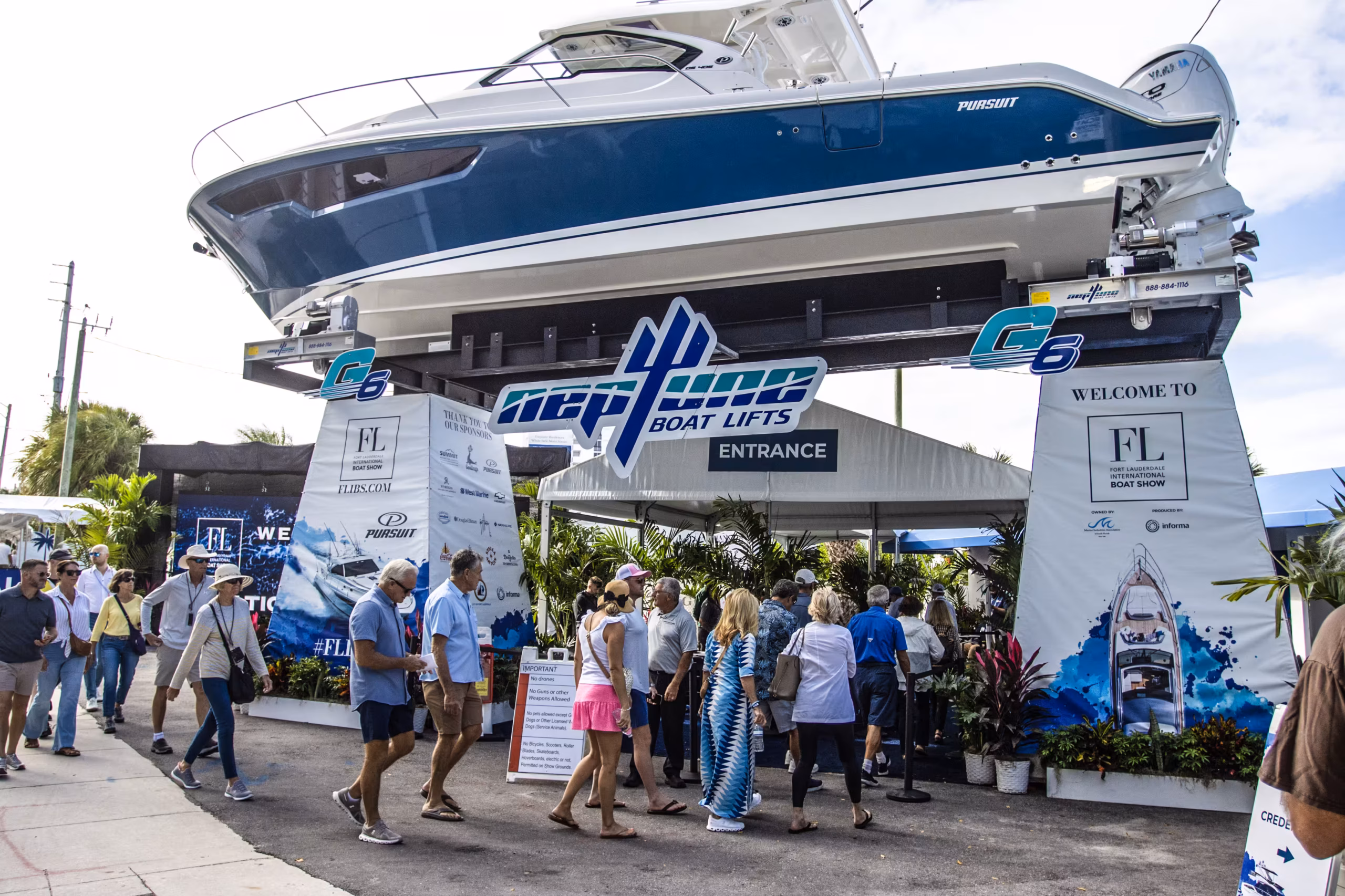 Visitors entering the Fort Lauderdale International Boat Show beneath a Pursuit sport yacht raised above the gate on a boat lift